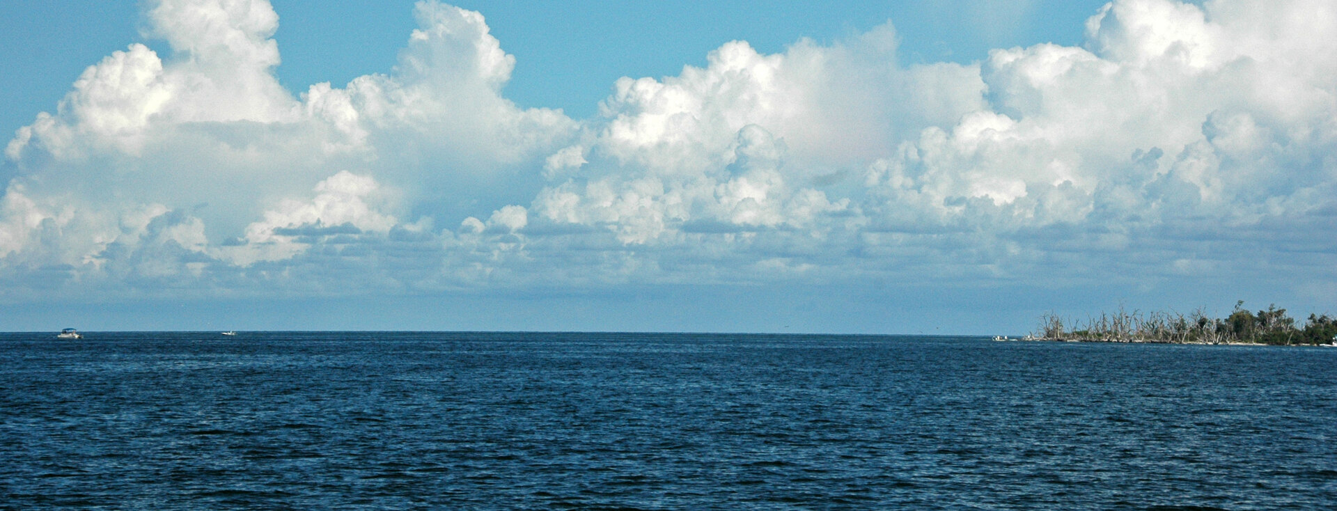 Small boats under way on the open water of Pine Island Sound near Captiva Pass, Southwest Florida, with a barrier island on the horizon