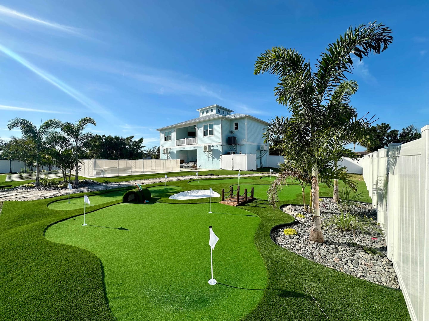 The rear grounds at Seaside Boca, a Travel DRD home in Placida, Florida, with a putting green, palms and the pool cage behind